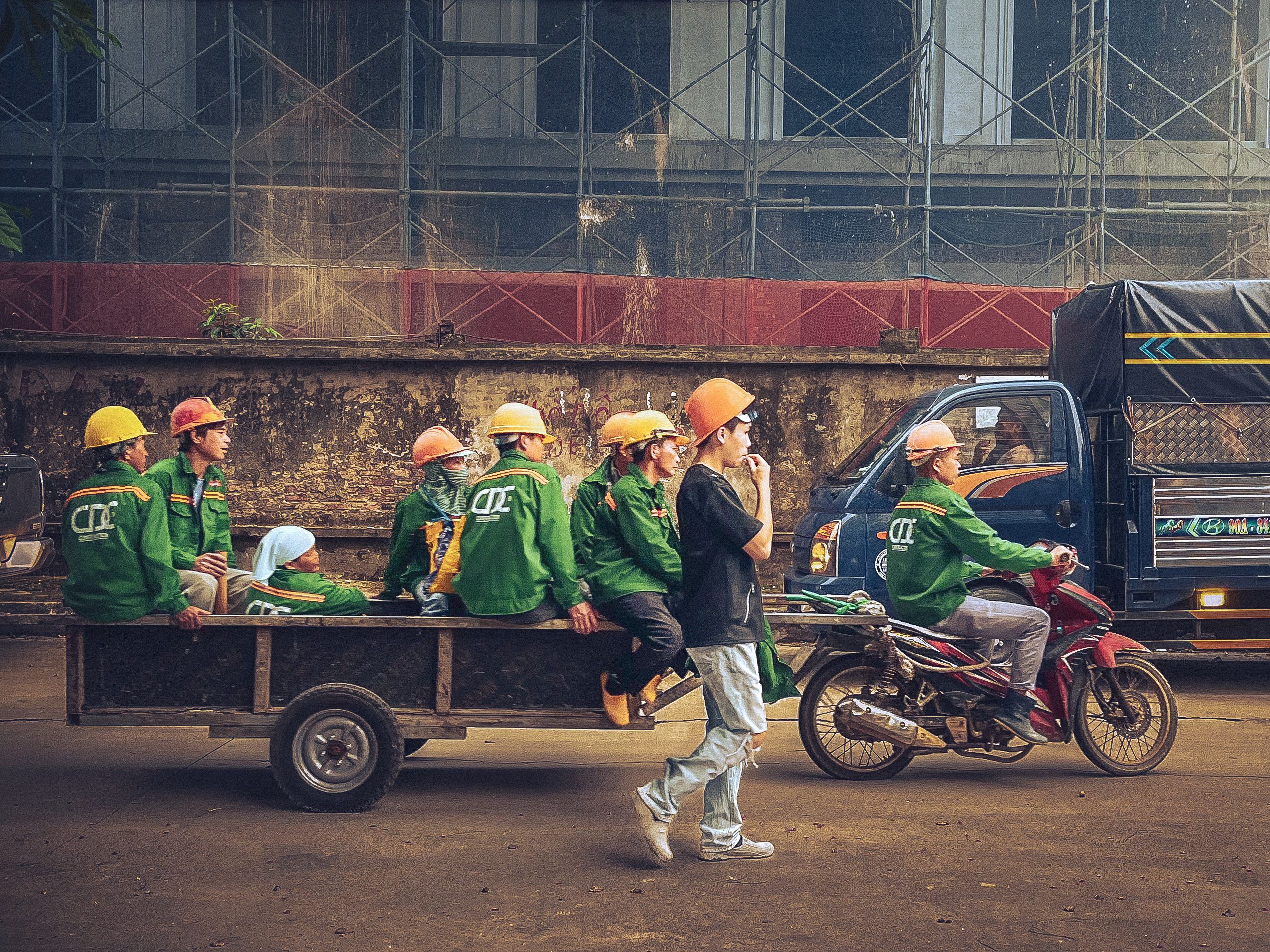 A motorcycle pulls a cart full of construction workers in an urban setting, showcasing teamwork and industry.